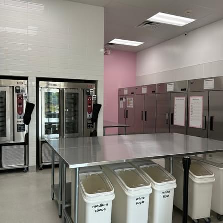 A wide shot of the customer-facing counter of a newly-construced Crumbl cookie franchise. It's black and white with pink accents, cookie illustrations and a white counter and cabinetry.
